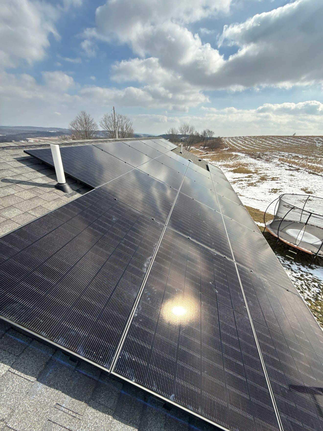 Solar panels on a shingled roof overlooking open winter fields