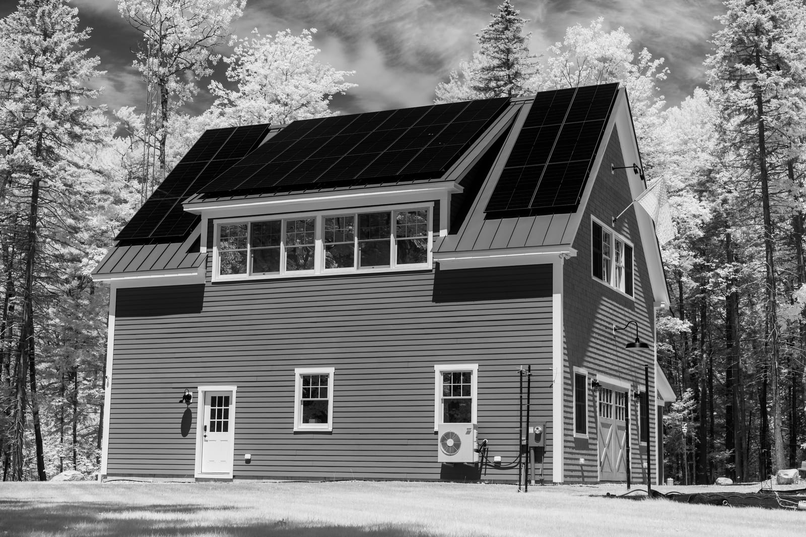 Shingled two-storey home with dark roof-mounted solar panels among snowy trees