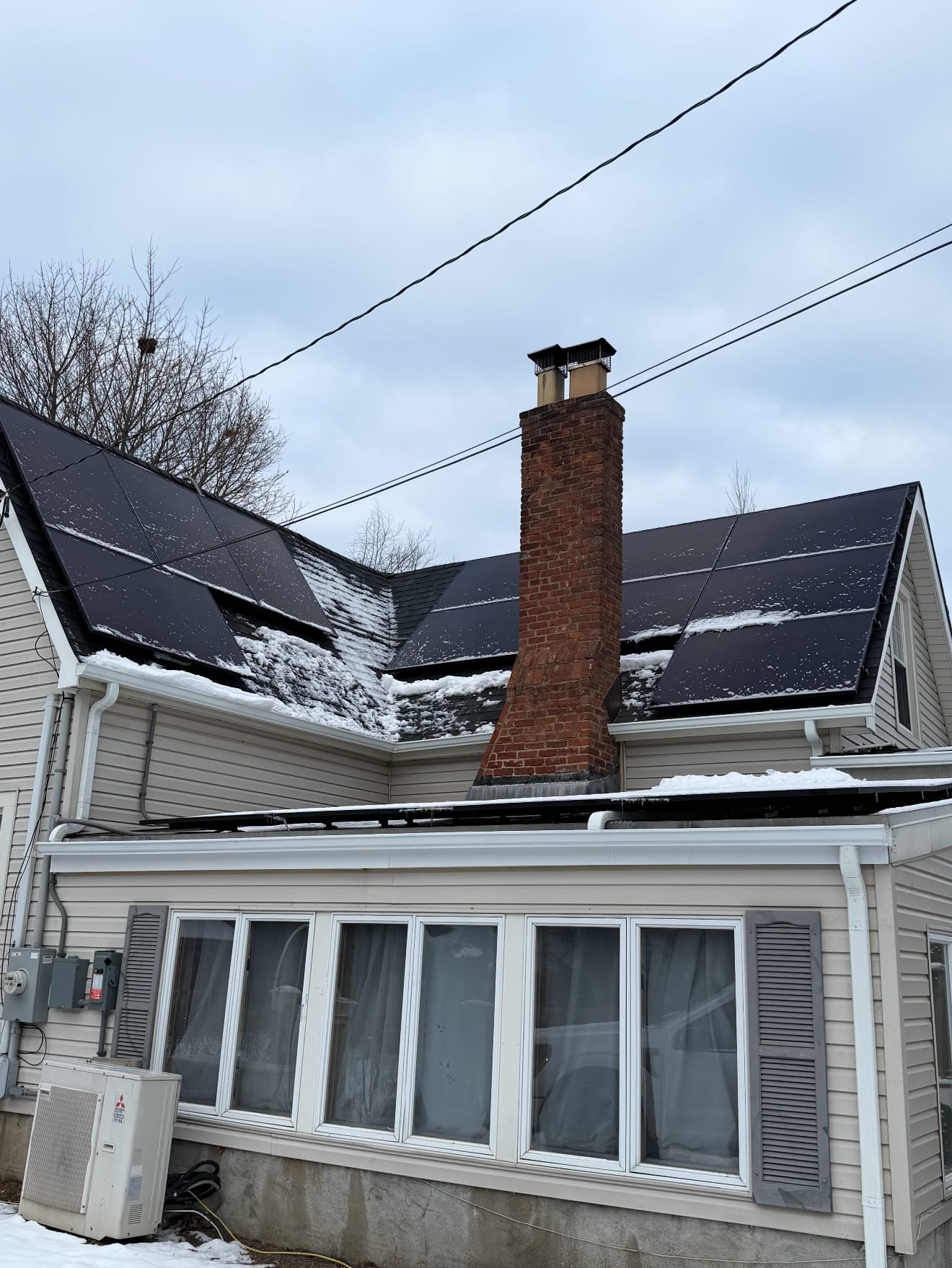 Black solar panels on the dormered roof of an older home with a brick chimney